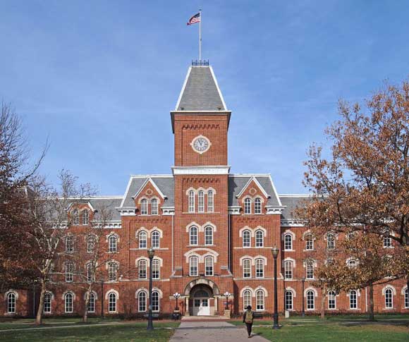 red brick college building with tall steeple with a clock face and flag on top