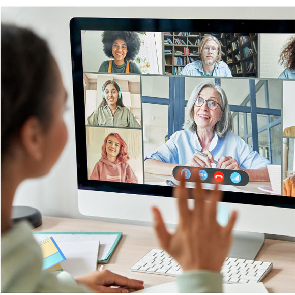 computer screen showing multiple people in an online meeting with blured foreground image of girl looking at screen and waving