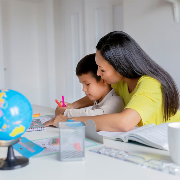 Asian boy and mom doing homework at table with globe in foreground