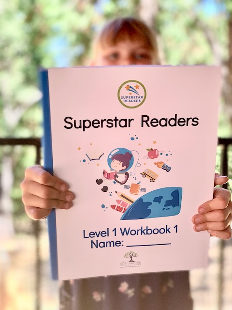 Girl holding Superstars Readers book straight out in front of her