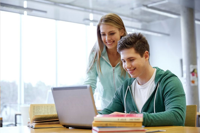 familyhomestudy boy sitting at desk with open laptop computer in front of him with woman standing next to him