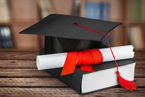 photo of a mortarboard on a table with a book and a rolled diploma in front of it