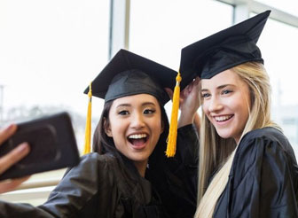 two girls in black caps and graduation gowns taking a selfie