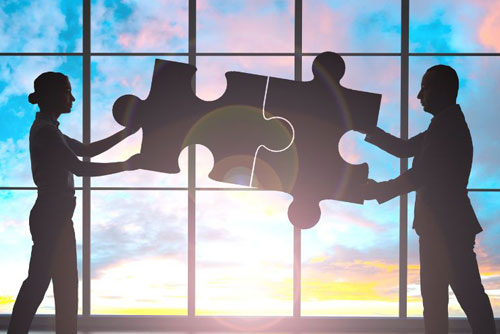 graphic of a man and woman holding giant interlocking puzzle pieces in front of a large window with a sunset
